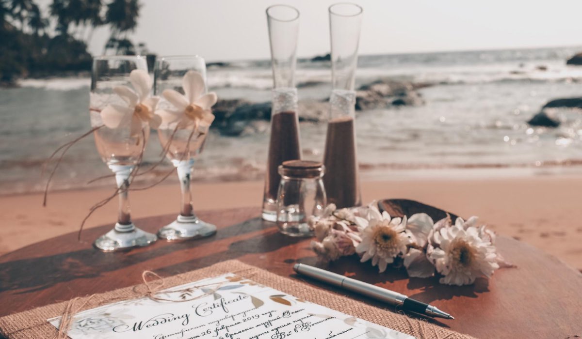 wedding certificate, two glasses and some flowers on a table next to a beach