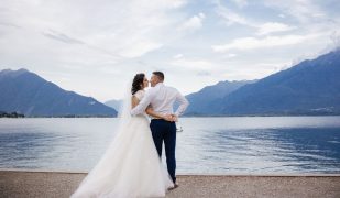 wedding couple standing in front of mountains and a large body of water while embracing