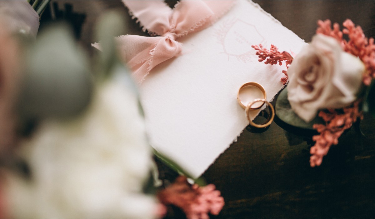 wedding invitation on a table with flowers and two wedding rings