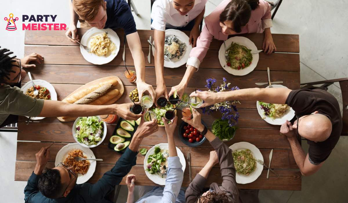 An overhead shot of a group of friends clinking glasses over a table set with food.