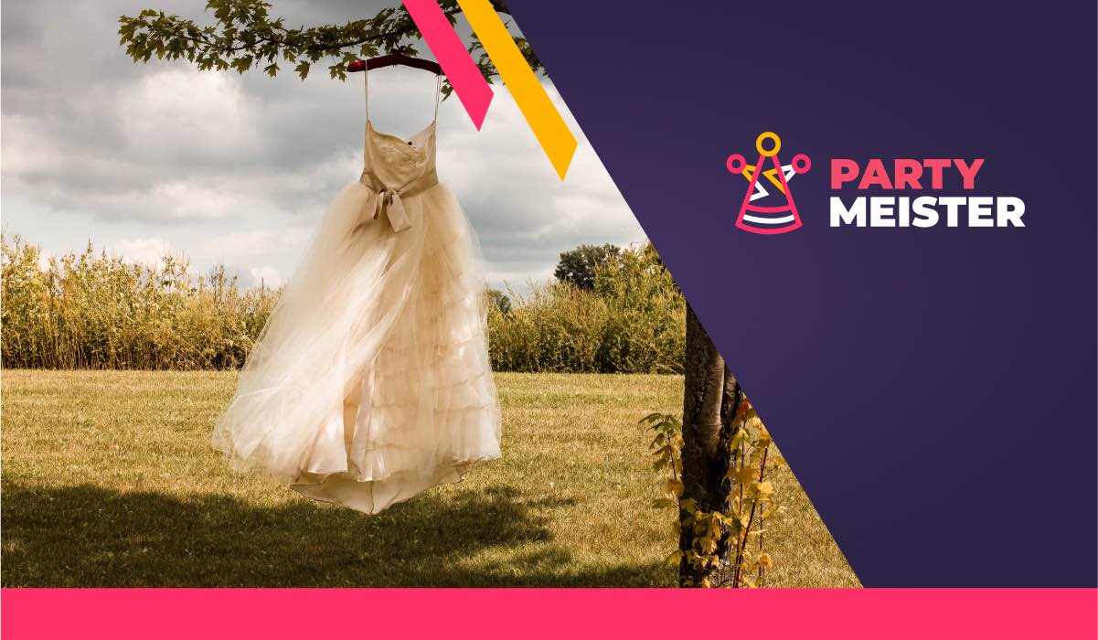 A wedding dress hanging on a branch of a tree by straps. The tree is growing on a large green field. There's a PartyMeister logo in the corner